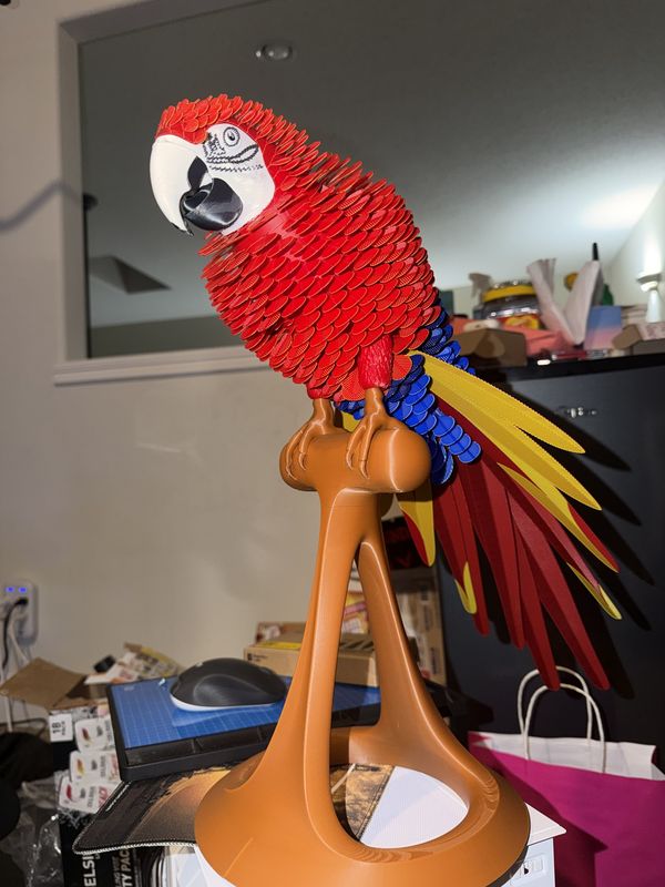 Red, blue and yellow 3D-printed scarlet macaw with layered feathers, standing on a perch