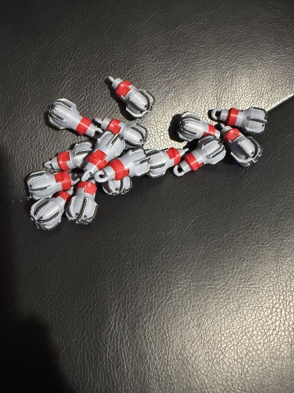 Pile of small gray and red 3D-printed PDC drill bit keychains