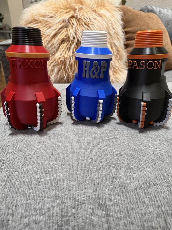 3D-printed PDC drill bit replicas in company colors on a desk