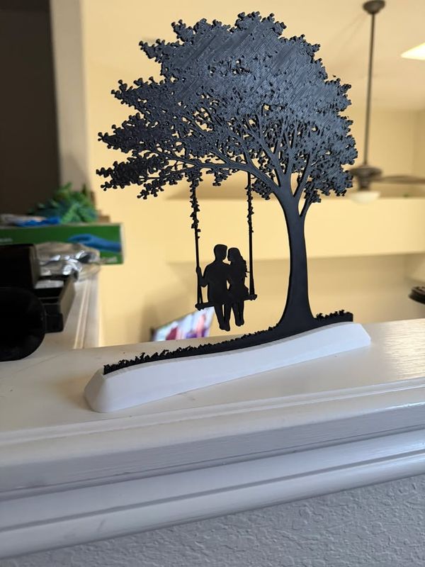 3D-printed silhouette of a couple on a swing under a tree, standing on a shelf
