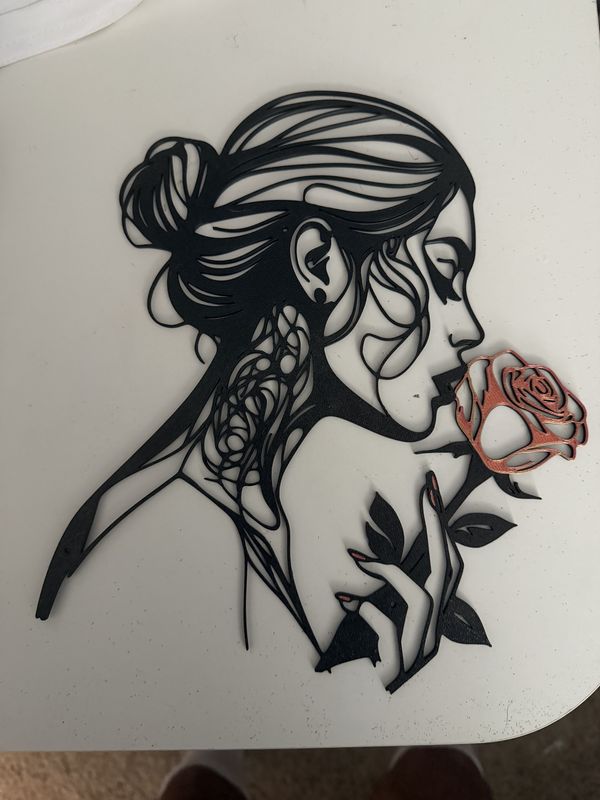 Black 3D-printed silhouette of a woman smelling a copper rose, wall art